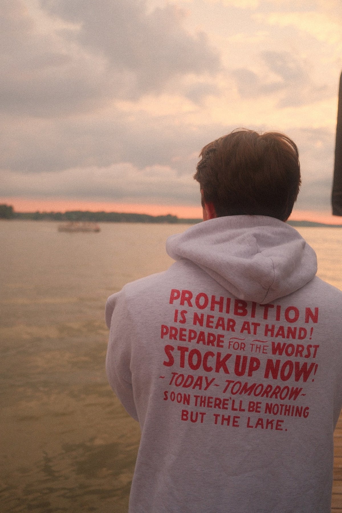 Light grey Ohio Anti-Saloon League Nothing But The Lake oversized hoodie worn by a lake at sunset, back graphic in red